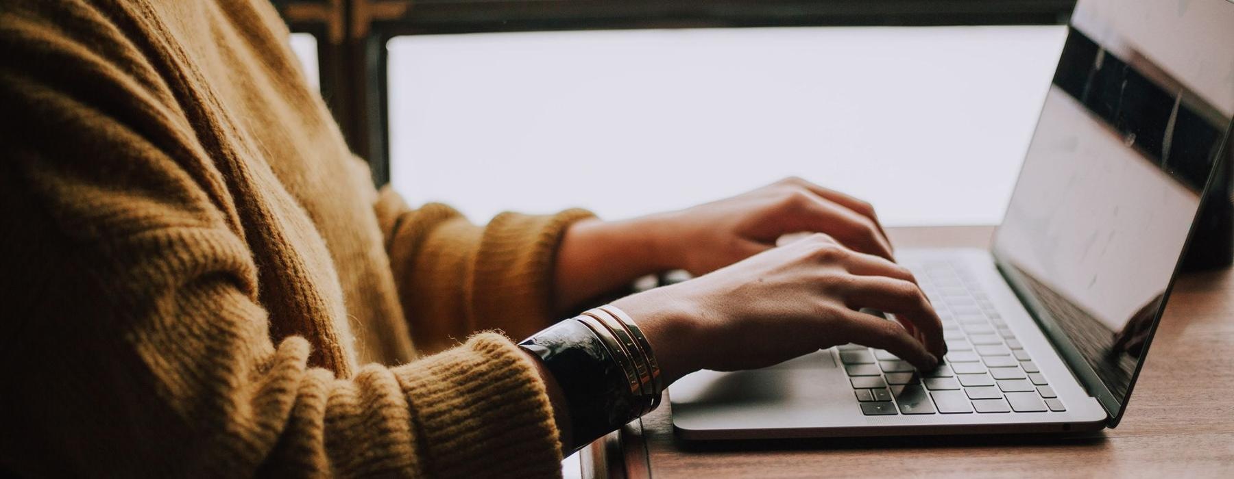 woman types on her laptop near large window