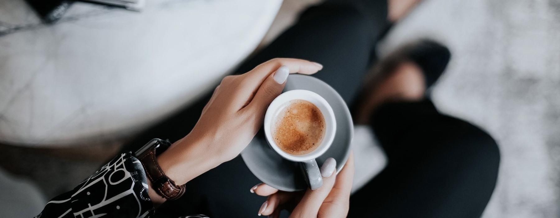 business woman sits next to a marble table with books and holds a saucer with a cup of espresso